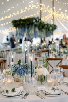 the table is set with white and blue flowers in vases, candles, and napkins