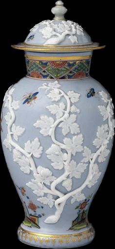 a large blue vase with white flowers and birds on it's lid, sitting in front of a black background