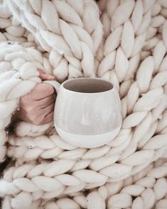 a person is holding a coffee cup in their hand while wrapped up in a blanket