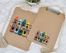 two brown notebooks with colorful crayons on them next to a beaded plant