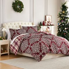 a bed with red and white comforter next to a christmas tree