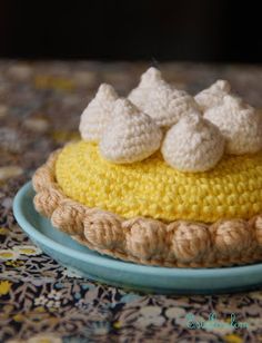 a crocheted cake on a blue plate with yellow icing and white marshmallows