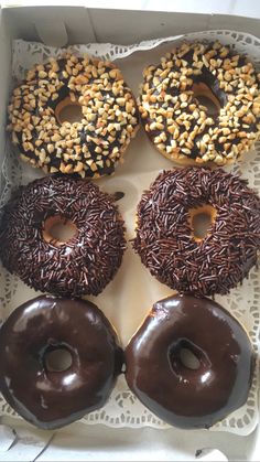 four donuts with chocolate frosting and sprinkles in a box