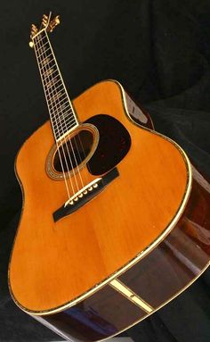 an acoustic guitar sitting on top of a black cloth covered case with the strings still attached