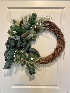 a wreath with pine cones and greenery hangs on the front door's wall