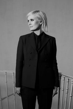 a woman in a black suit and tie standing on a stair railing with her hands in her pockets