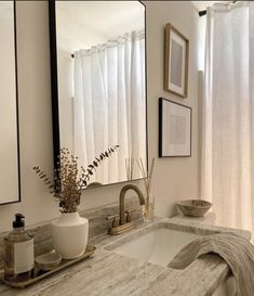 a bathroom sink under a large mirror next to a window with white drapes on it