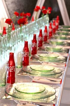 coca - cola bottles are lined up on a long table with plates and glasses in front of them