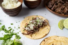 three tacos with meat, onions and cilantro on a table next to other food