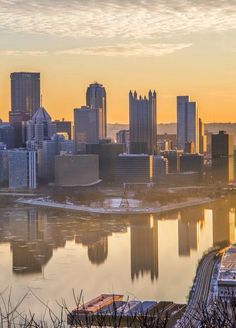 a city skyline is shown with the sun setting in the background and water reflecting off it's surface