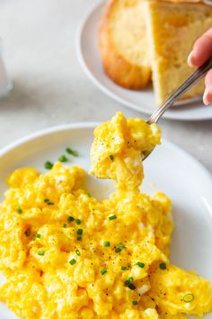 someone is eating scrambled eggs on a white plate