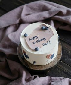 a birthday cake with blueberries on it sitting on top of a wooden table next to a pink blanket