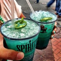 two people holding up green drinks with straws and pickles on them in their hands