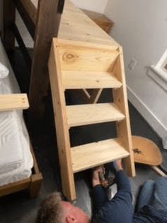 a man laying on the floor next to a wooden bunk bed with shelves underneath it