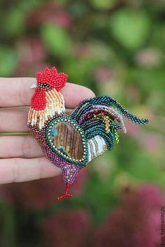 a hand holding a small brooch with a rooster on it's back and a heart in the middle