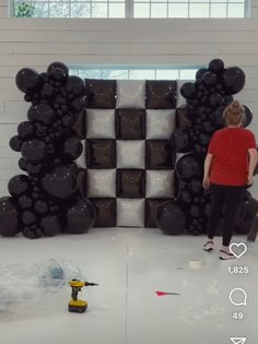 a young boy standing in front of a wall made out of black and white balloons