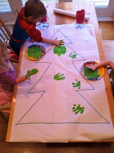 two children sitting at a table with paper plates and handprints on the table