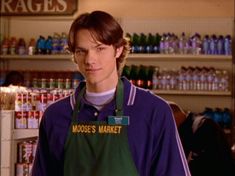 the young man is wearing an apron and standing in front of shelves