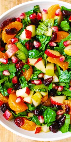 a white bowl filled with spinach, oranges and cranberry salad on top of a wooden table