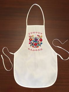 an apron with embroidered flowers on it sitting on a wooden table next to a pair of scissors