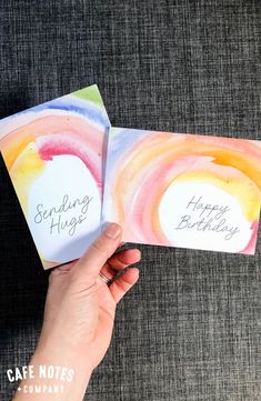 someone is holding two birthday cards with the words sending hugs and happy birthday written on them