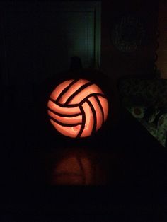 a lit up pumpkin sitting on top of a table in the dark with a volleyball ball carved into it