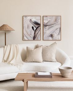 two paintings hang on the wall above a white couch and coffee table in a living room