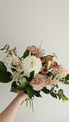 a hand holding a bouquet of flowers on a white background with greenery in the foreground