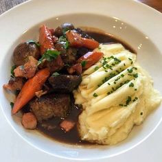 a white plate topped with mashed potatoes, meat and veggies covered in gravy