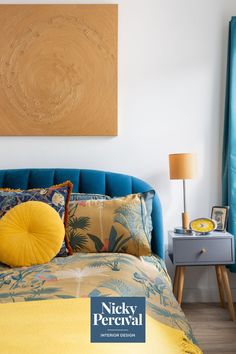 a bed with yellow and blue pillows in a bedroom next to a painting on the wall