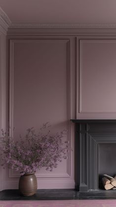 a vase filled with purple flowers sitting on top of a table next to a fireplace