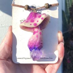 a hand holding a purple and white glass bead with a pink flower on it