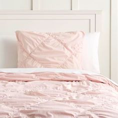 a bed with pink comforter and pillows on top of it in a white room