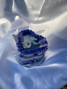 a blue and white cake sitting on top of a bed covered in white cloths