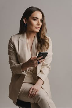 a woman sitting on top of a stool holding a cell phone in her hand and looking at the screen