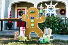 a large gingerbread man standing in front of a house with presents on the ground