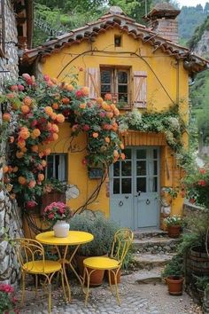 a yellow table and chairs in front of a house with flowers growing on the walls