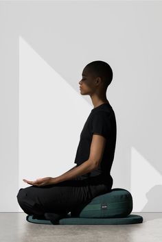 a man sitting on the ground in front of a white wall with his hands together