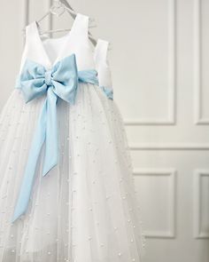 a white and blue dress hanging on a hanger with a light blue bow at the waist