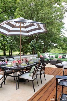 an outdoor dining area with table, chairs and umbrella on the deck in front of trees