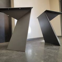 two metal sculptures sitting on top of a cement floor next to each other in an empty room