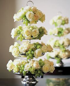 three tiered cake stand with flowers and grapes on each tier, in front of a window