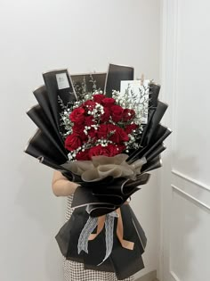 a bouquet of red roses is wrapped in black paper and tied to a white wall