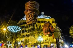 the building is lit up at night with bright lights on it's sides and large sculptures in front