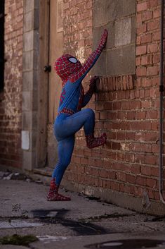 a person in a spiderman costume leans against a brick wall and reaches for something