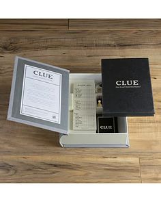 an open box containing the contents of a clue book on a wooden floor with a notepad and pen next to it