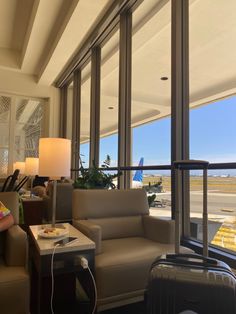 a living room with couches and luggage in front of large windows overlooking an airport