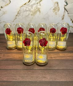 six glass vases with flowers in them on a wooden table next to a marble wall