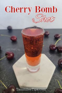 a glass filled with cherry bomb shot sitting on top of a marble coaster next to cherries