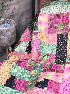 a colorful patchwork quilt sitting on top of a wooden chair next to a potted plant